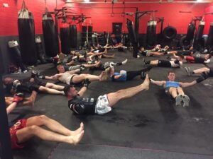 Raptors Muay Thai members performing core strengthening exercises during a group fitness class, focusing on form and endurance.